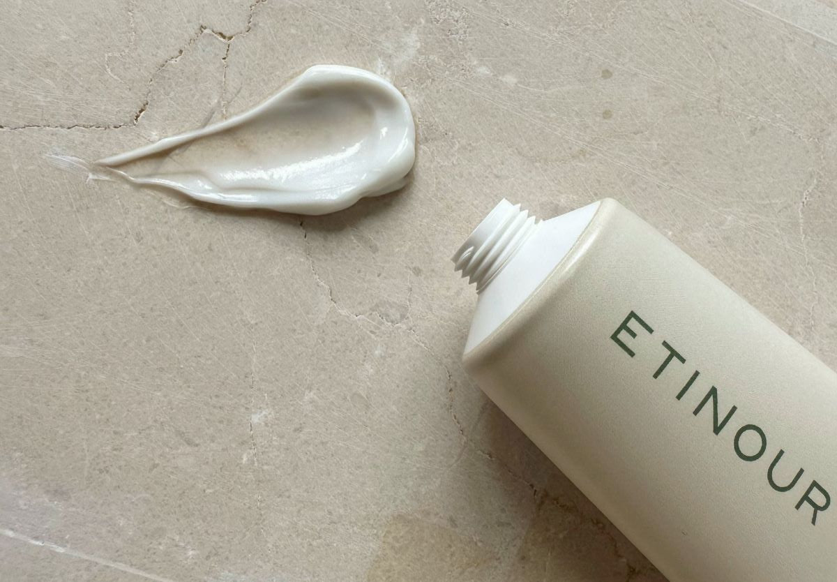 Close-up of Etinour's beige Essential Whitening Toothpaste tube on light stone with formula pressed out on the side. 